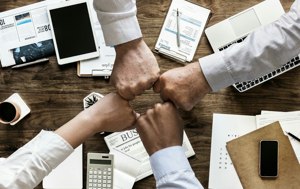 4-way fist bump over a work conference table. Header image for "small business in mind"